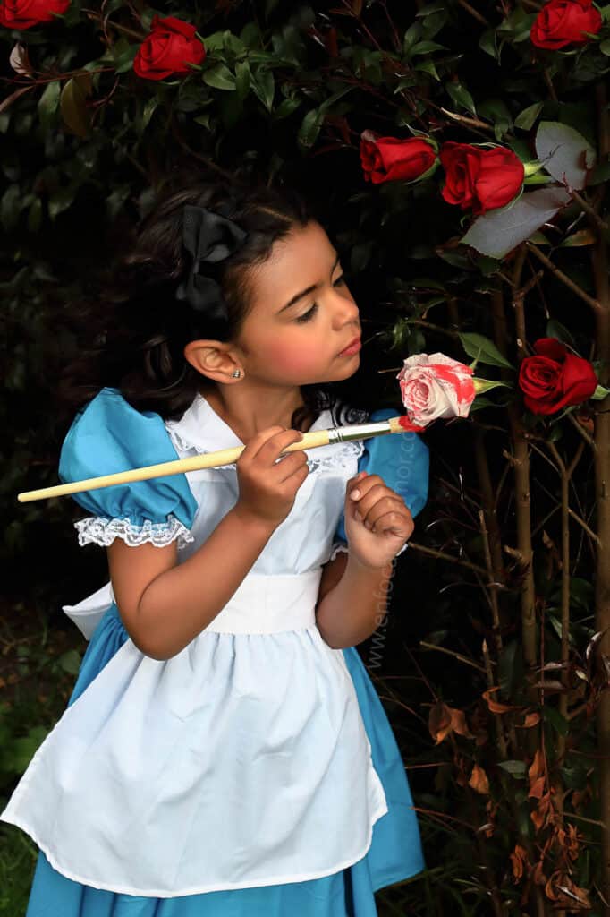 guía de fotografía para mamás. fotografia niña recreando la escena de  alicia en el país de las maravillas  pintando rosas blancas de rojo.